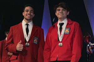 Two Multimedia students in red jackets with thumbs-up and silver medals